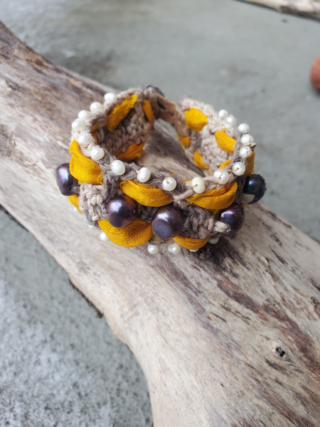 The base of this fiber bracelet is crocheted with a greyish hemp cord.  I thread the yellow Sari silk ribbon though the eyelets on both sides of the base, hand stitched tiny white pearls long the edges, and larger peacock pearls along the center. 