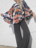 Person wearing a tie-dye jacket and black pants against a light gray wall.