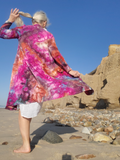 Person wearing a colorful tie-dye jacket on a beach with rocks and sand. A back shot