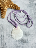 Adjustable lilec cord crocheted necklace with a white shell pendant on a textured surface