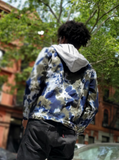 A man's denim jacket with a removable hood. Tie dyed in earthy navy-olive colors. The  jacket is cotton, and the tie dye colors look great on it, but the hood is a poly material, and did not take the dye. It remains an ash grey sweatshirt fabric and color. Our frined daniel is the model for this style; this first photo is of his back.