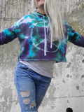 I'm modeling this cute raw edge crop hoodie; there is a glue resist dawn peace sign on the front, drawstrings around the hood, ribbed cuffs on the sleeve ends. Tie dyed in purple-green-jade-black. I have a longer white tank top under and distressed jeans