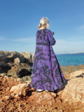 Person wearing a long, patterned dress standing on rocky terrain with ocean and sky in the background
