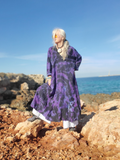 Person wearing a purple dress sitting on rocks by the ocean
