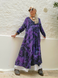 Person wearing a purple tie-dye dress standing against a textured wall.