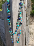 Necklace with blue and green beads hanging on a wooden post.