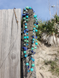 Necklace with blue and green beads hanging on a wooden post outdoors.