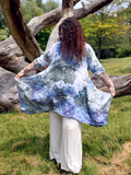 Person wearing a tie-dye dress standing in a natural setting with trees and grass.