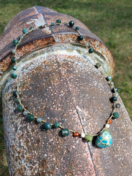 a dainty choker photographer on a rusty pipe: it is made with tiny moss agate beads, a bit of accent orange, white and green gems, and an added larger pebble fical bead in the center, which is a pretty turquoise seas sediment bead