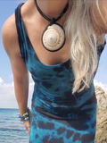 Person wearing a blue tie-dye dress with a large necklace by the ocean