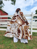 Dena is standing front of a white fence; this photo is showing the back of the lightweight duster cardigan.. Dena has her hands in the cardigan's pockets
