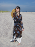 Steph has the cardigan fronts wrapped across her body, holding them with one arm, the otherone is on her side. She also has sunglasses and a straw hat hanging behind her.