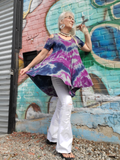 I'm modeling a size small cold shoulder tunic; I hand dyed the heather gray garment in navy 7 purple colors.  The tunic top has short sleeves with the coulder cut outs, a formfitting shape across the chest, and a flowy swing detail down for the rest . This shot is in the motion, "floating" around me. White bell bottoms and shell necklaces complete the look,. Oh, and large silver spiral earrings.