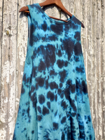 Blue tie-dye sleeveless dress hanging on a wooden hanger against a rustic wooden background.