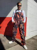 Person wearing tie-dye overalls standing against a red and white wall.