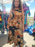Woman wearing a tie-dye dress standing in front of a clothing stall with tie-dye garments.