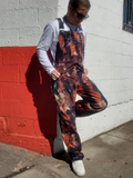 Person wearing tie-dye overalls against a red and white wall.