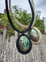 Two necklaces with abalone shell pendants hanging against a blurred natural background. black or ecr cord