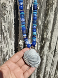 Necklace with blue beads and a shell held against a wooden background