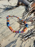 Colorful beaded necklace on a sandy surface with driftwood