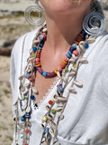 Person wearing a colorful necklace with shells and beads on a blurred natural background