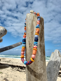 Colorful beaded necklace on a wooden post with a beach and ocean background