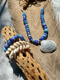 Necklace with blue and white beads and a shell on natural wood and stone background
