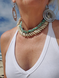 Person wearing a necklace and earrings with a beach background