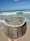 Coconut shell with turquoise and beige beads held on a beach