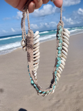 Necklace with shell and bead details held over a beach