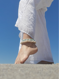 Person wearing a white outfit, a shell anklet with a clear blue sky background