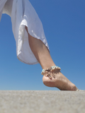 Foot wearing a anklet with a clear blue sky background