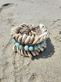 A handmade shall-beaded anklet, resting on sandy ground.