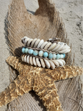 chunky shells and amazonite beads anklet placed on a starfish prop, featuring white cowrie shells, light blue beads, and white shells, set against a sandy beach background.