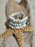 A chunky layered beach anklet displayed on a dried starfish over sand.