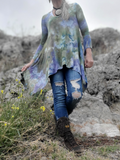 Person wearing a tie-dye shirt and ripped jeans standing on rocky terrain with yellow flowers.