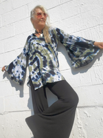 Person wearing a tie-dye shirt and dark pants against a white brick wall.
