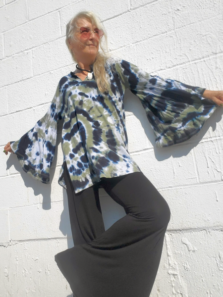 Person wearing a tie-dye shirt and dark pants against a white brick wall.