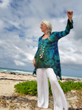Woman in a colorful top and white pants standing on a beach with ocean and sky in the background