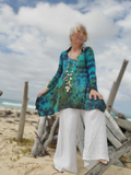 Woman in a colorful dress sitting on a beach with ocean and sky in the background