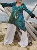 Person wearing a colorful top and white pants on a beach with driftwood in the background