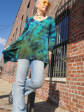Person wearing a tie-dye shirt and jeans standing against a brick wall.