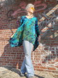 Person wearing a blue tie-dye shirt and light blue jeans standing against a brick wall with graffiti.