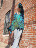 Person wearing a tie-dye shirt and light pants leaning against a brick wall.