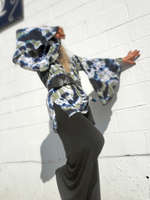 Person wearing a tie-dye outfit with a hood against a white tiled wall.