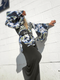 Person wearing a tie-dye outfit with a hood against a white tiled wall.