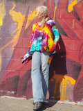 Person wearing a tie-dye jacket standing in front of a colorful graffiti wall.