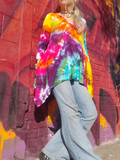 Person wearing a tie-dye shirt and jeans standing in front of a colorful graffiti wall.