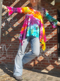 Person wearing a tie-dye shirt and jeans standing against a brick wall.