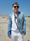 Man wearing sunglasses and a blue patterned jacket on a beach